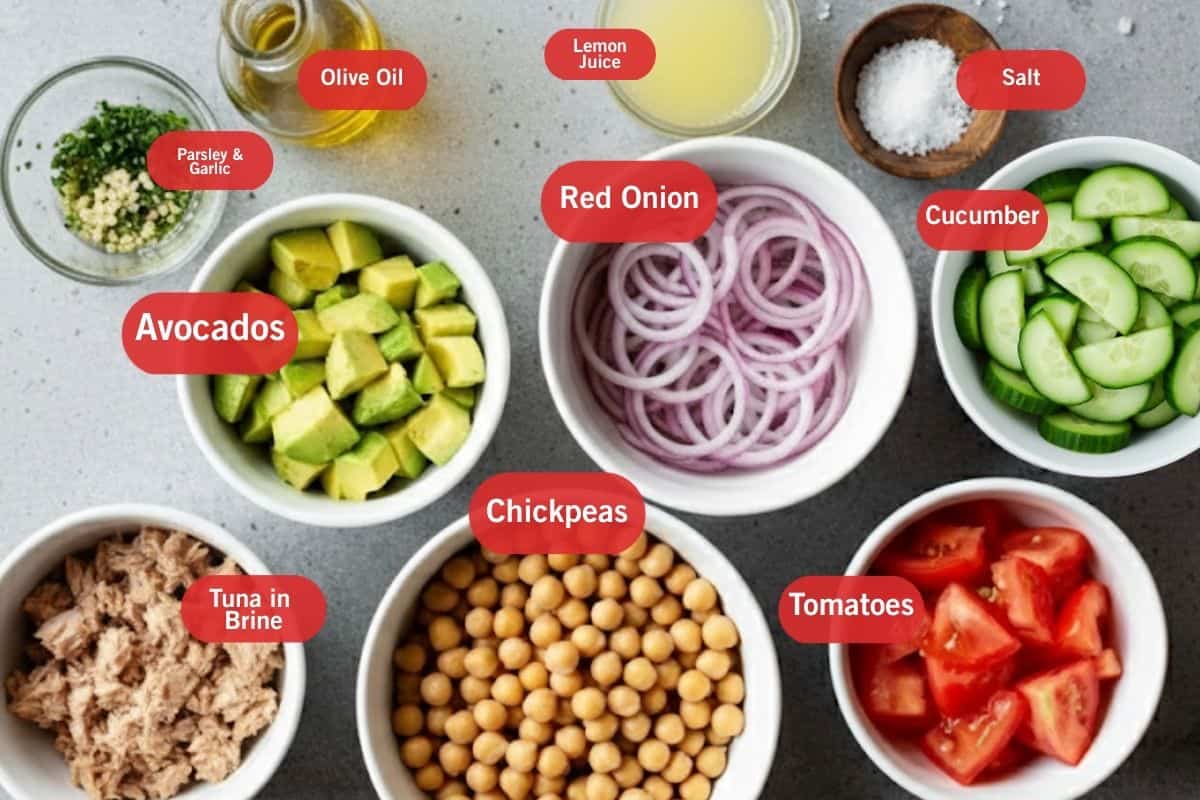 Flat lay photo of ingredient shot of parsley and garlic, olive oil, lemon juice, salt, cucumber, red onion, avocados, tuna in brine, chickpeas, tomatoes, cucumber