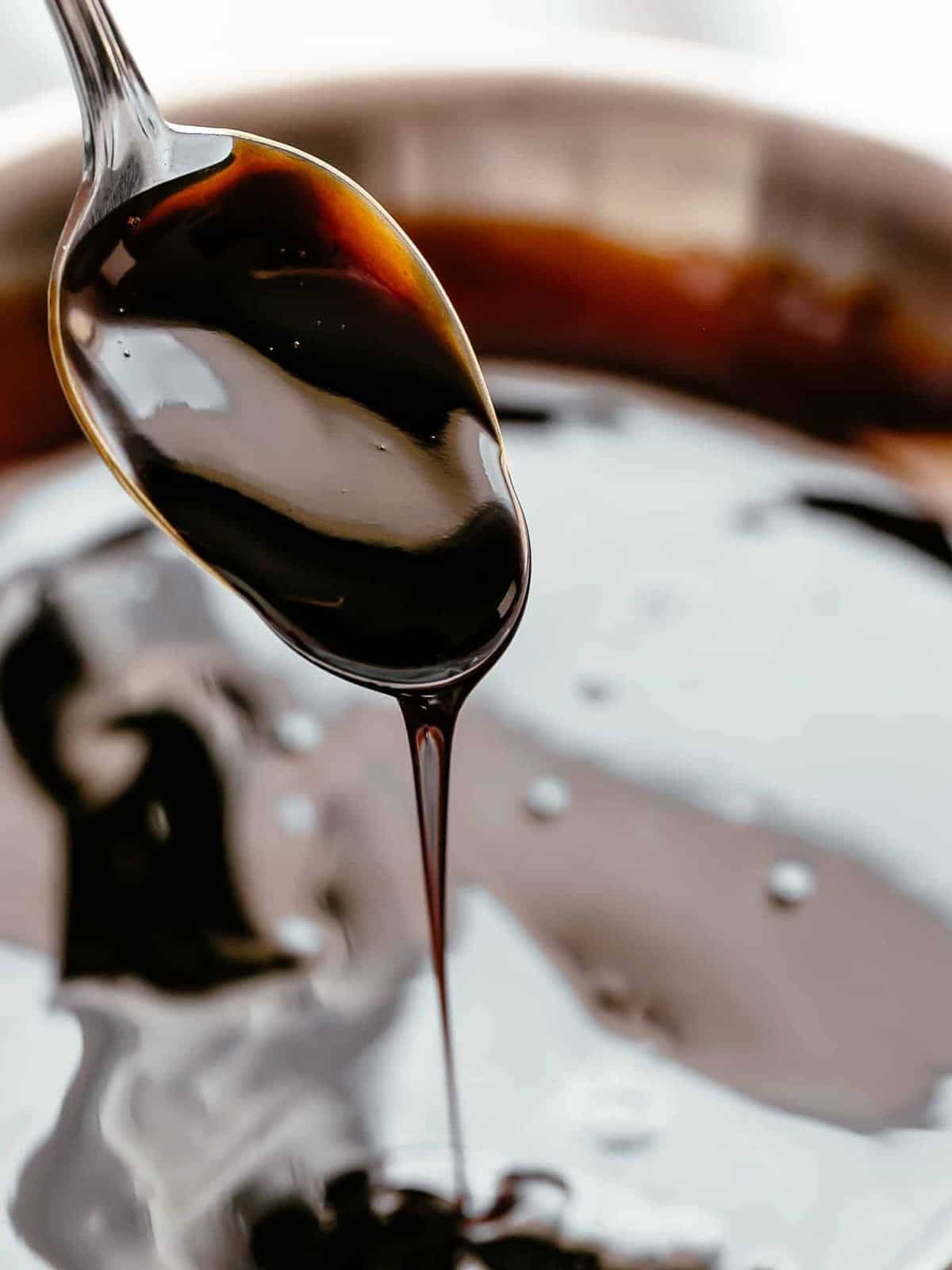 Thick, dark balsamic glaze being mixed dripping off a silver spoon into a bowl