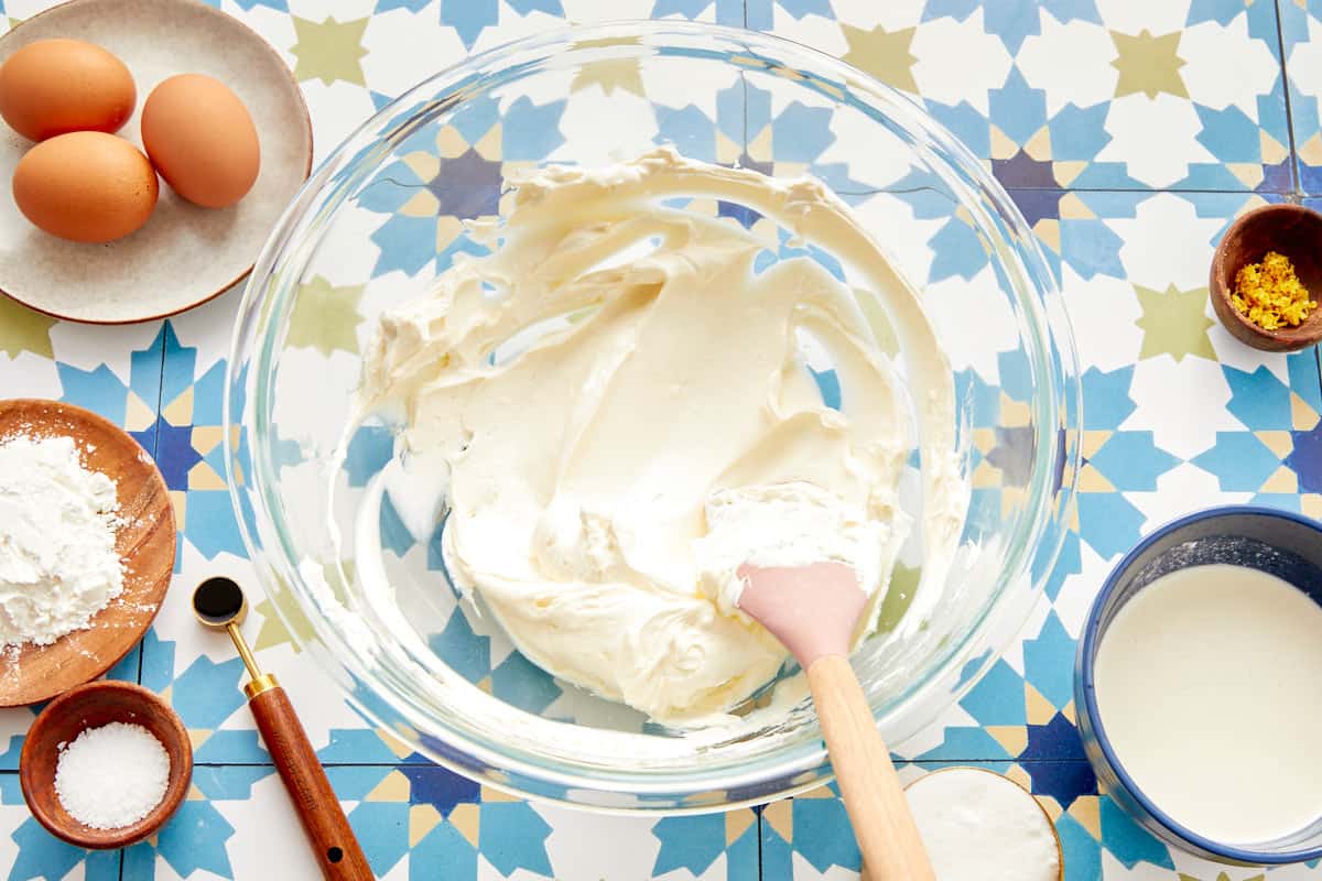 Cream cheese whipped smooth in a glass bowl with baking ingredients around it