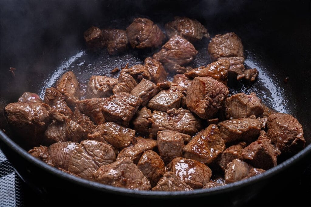 beef chunks being seared close up in a black pan