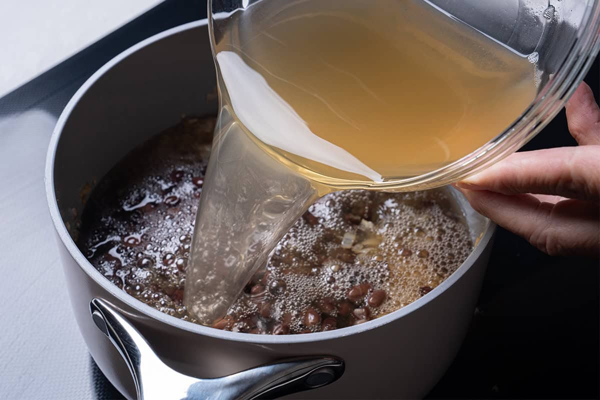 a pot with black beans inside heating having broth poured in
