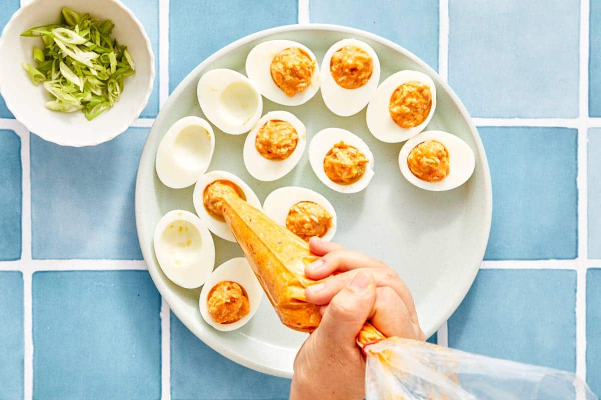 Piping the filling into egg whites on a platter.