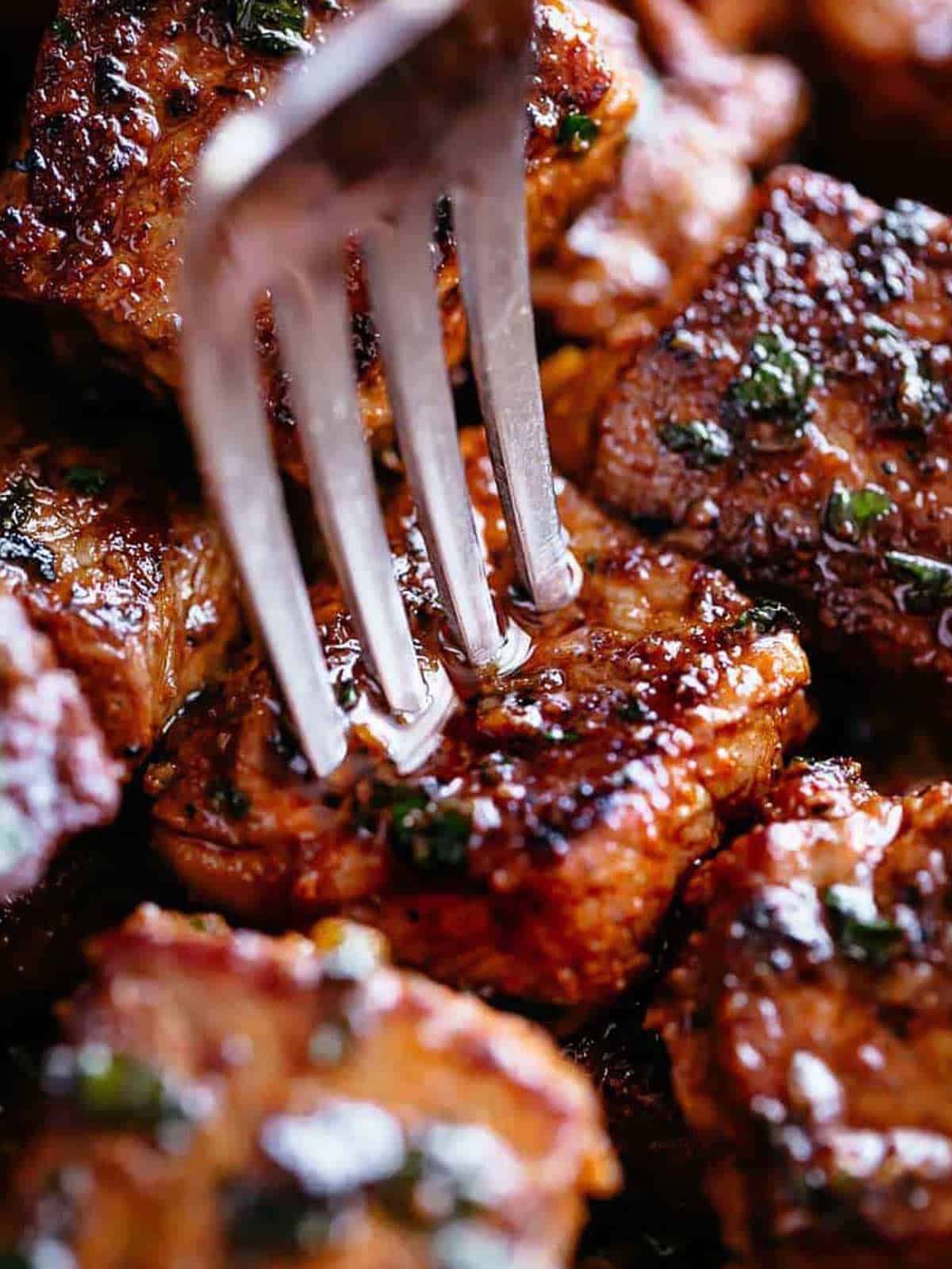 A silver fork pierces a steak bite with crispy edges