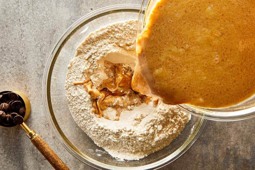 the pale brown colored substance being mixed into a dry ingredients mix in a bowl sitting on the table top