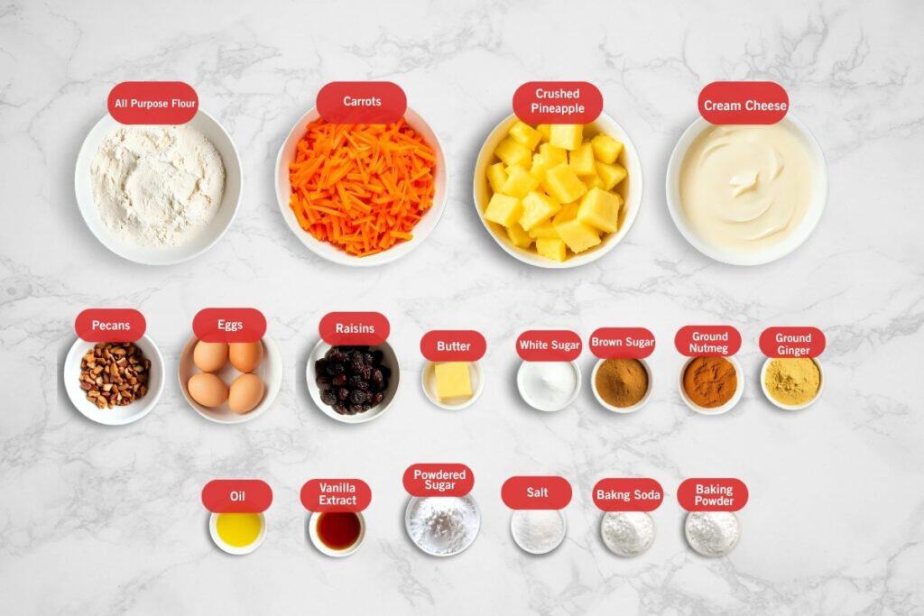 Flatlay image of carrot cake ingredients arranged in individual bowls on a white marble surface. Ingredients include all-purpose flour, shredded carrots, crushed pineapple, cream cheese, chopped pecans, eggs, raisins, butter, white sugar, brown sugar, ground nutmeg, ground ginger, oil, vanilla extract, powdered sugar, salt, baking soda, and baking powder.