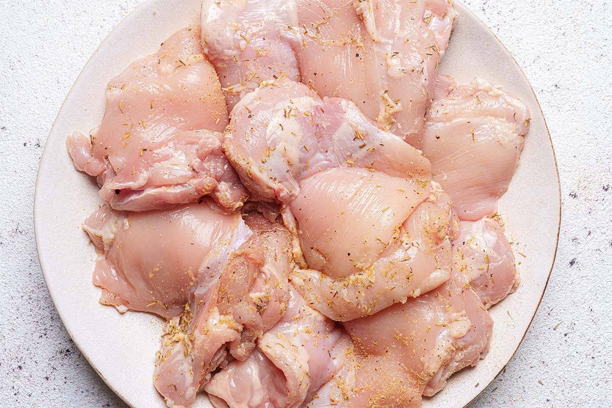 chicken sits on a white plate being coated with a seasoning