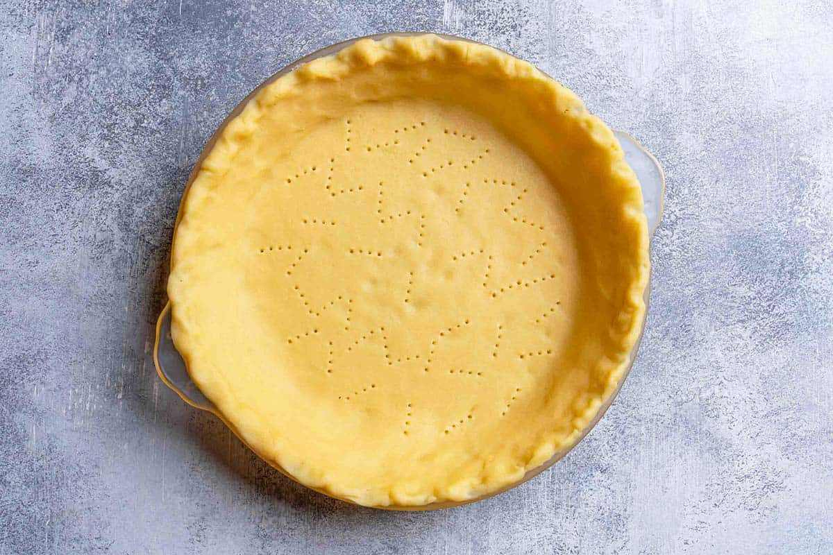 A pierced homemade pie crust base, perfectly laid in a baking dish, ready for the next good layer.