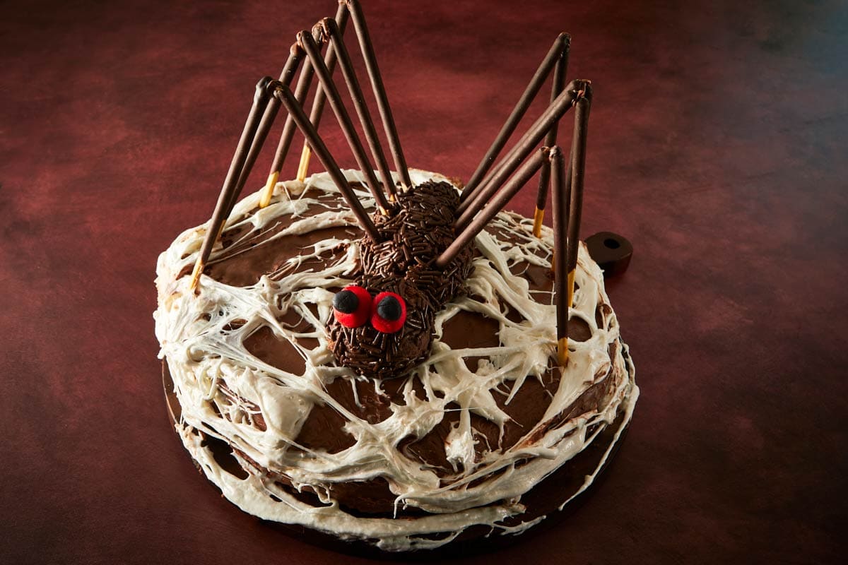 Assembling the spider on top of the cake, chocolate legs, red fondant eyes, and a marshmallow web.