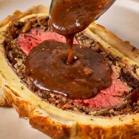 Beef Wellington slice with sauce being poured using a spoon.