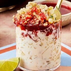 A glass of Esquites with a spoon and lime.