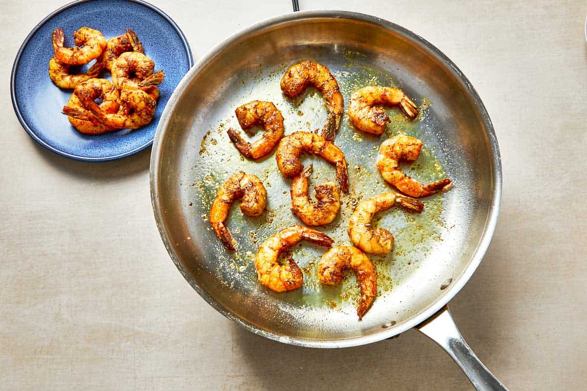 A frying pan with shrimp beside a colorful plate of food, showcasing a good meal.