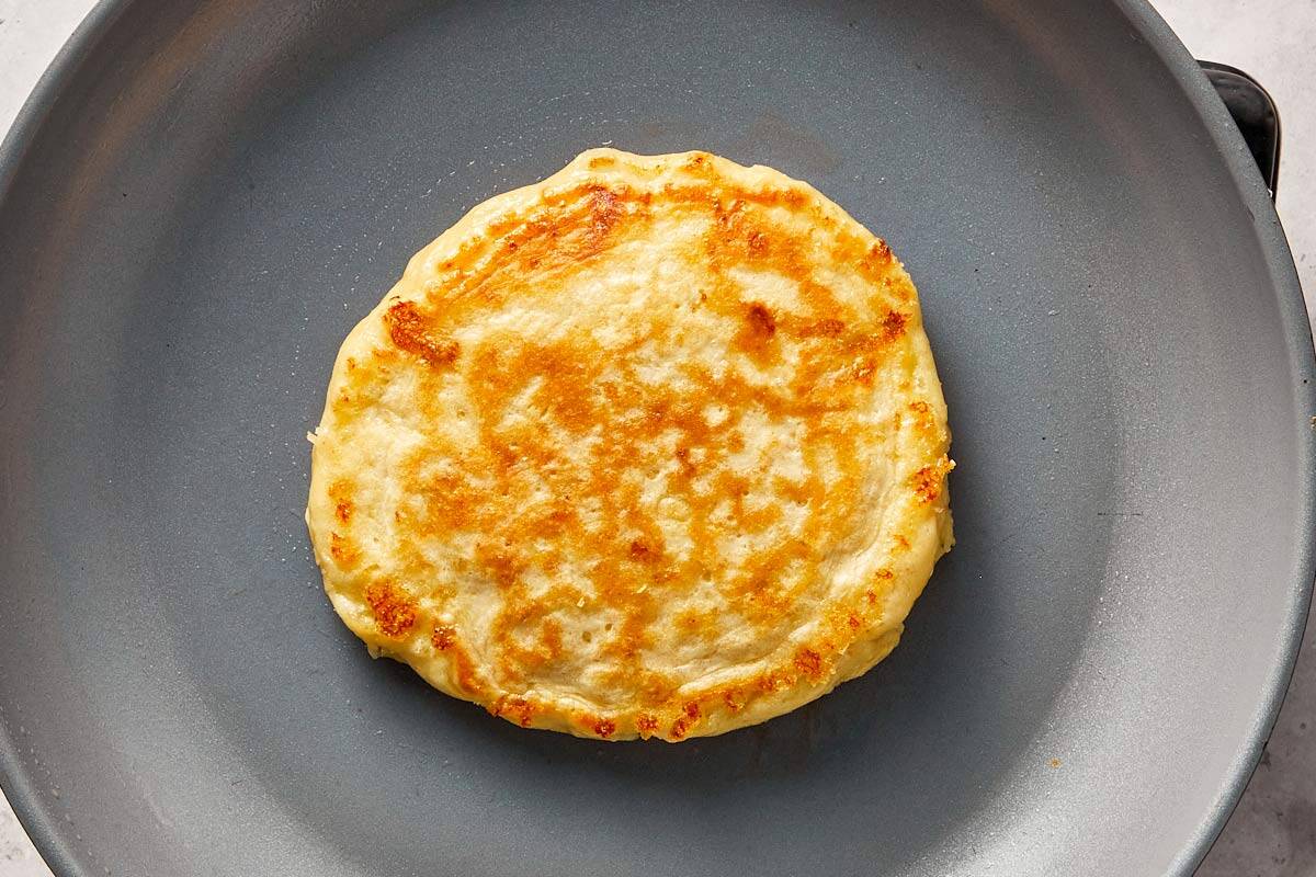 Cottage cheese pancake flipped and cooking on the other side, showing a golden brown surface.