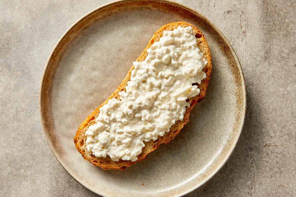 Cottage cheese spread over sourdough bread on a plate before air frying for cottage cheese toast.