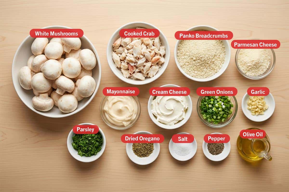 Top shot of ingredients: white mushrooms, cooked crab, panko breadcrumbs, parmesan cheese, mayonnaise, cream cheese, green onions, garlic, parsley, dried oregano, salt, pepper, and olive oil.