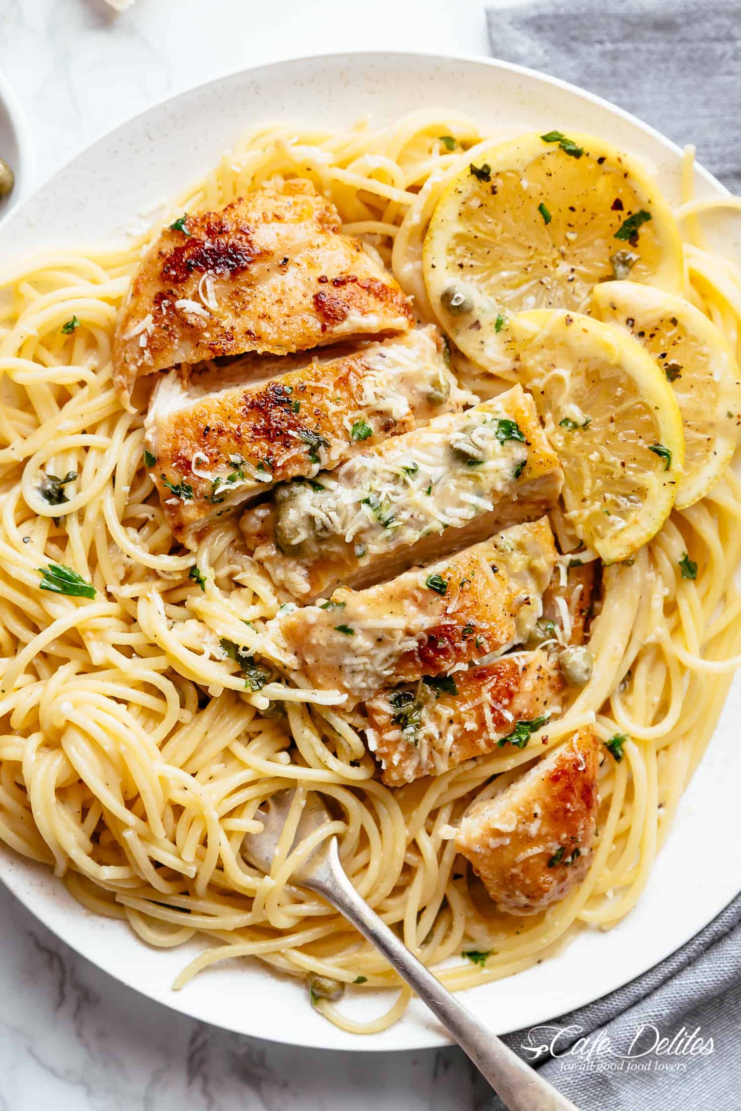 Creamy Lemon Parmesan Chicken sliced with some noodles on the sides on a plate