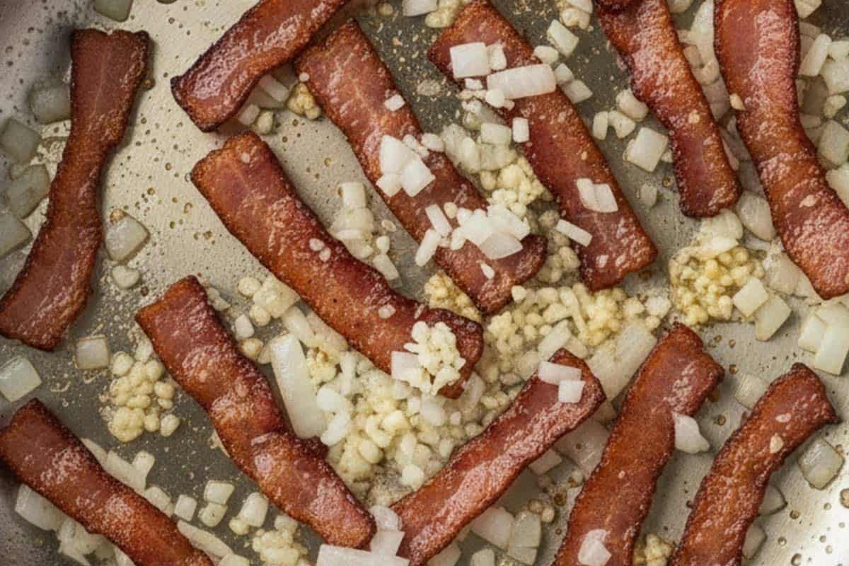 Cooking the bacon, garlic, and onon in a pan.