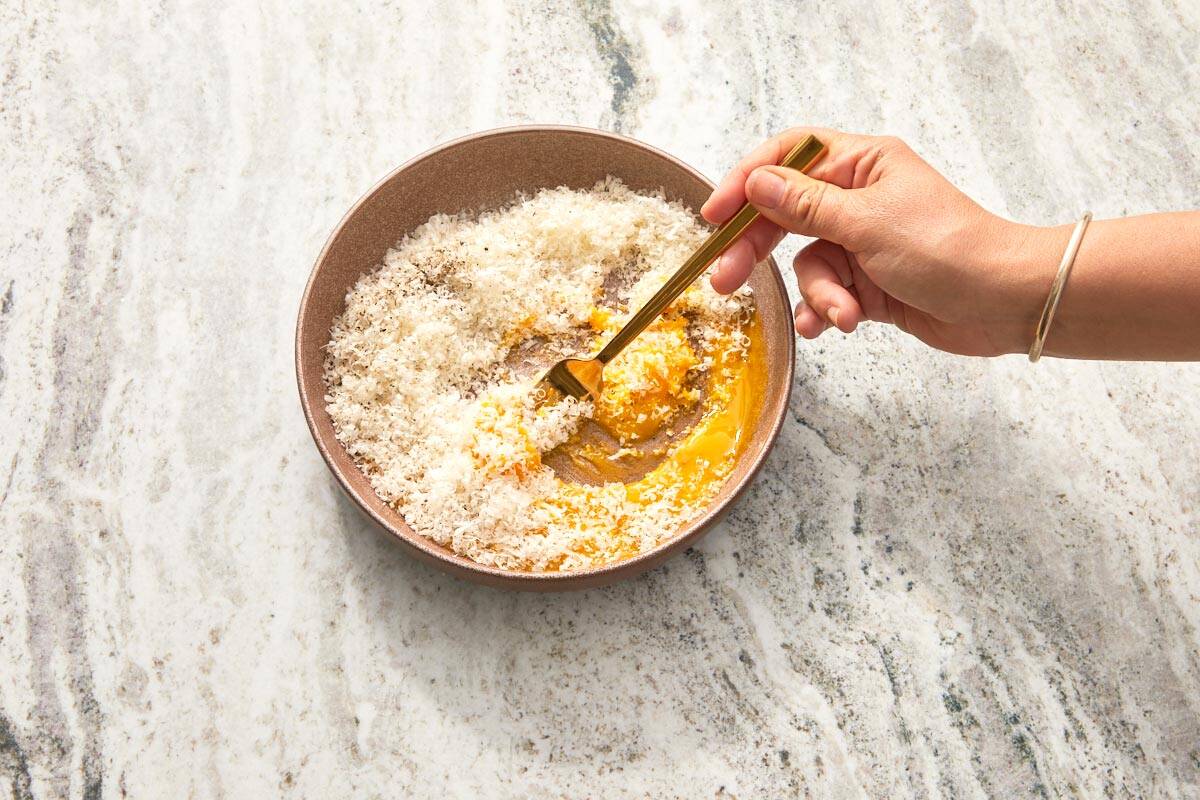 Grated Pecorino Romano being mixed with egg yolks and black pepper.