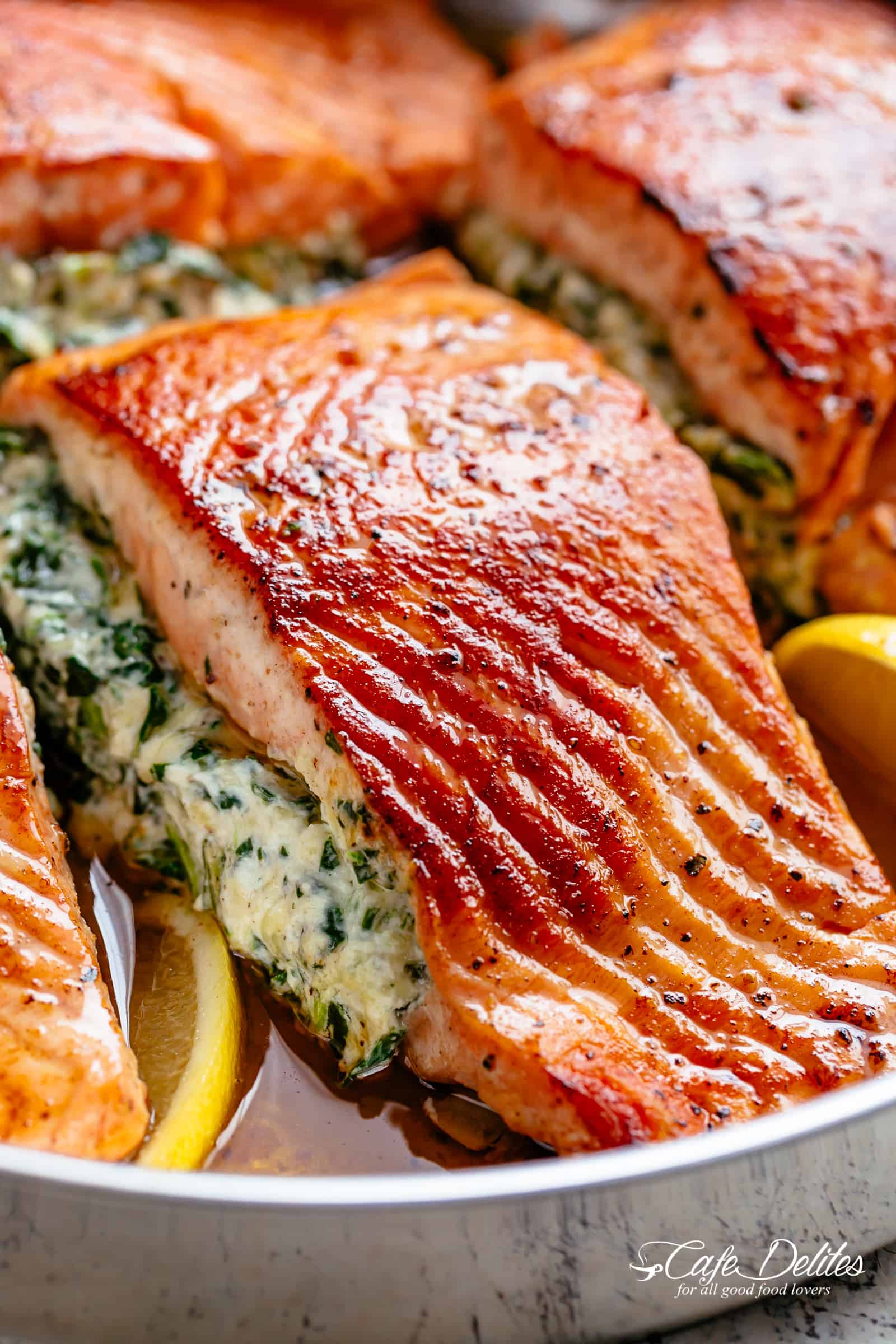 A close up image of a fillet of creamed spinach stuffed salmon in a silver pan with lemon slices