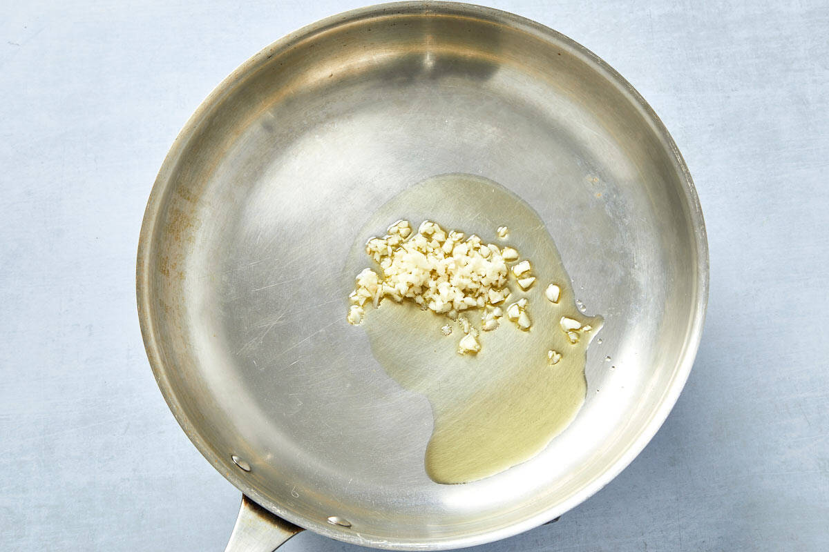 Garlic sizzling in olive oil in a pan, the first step in building flavor for creamy tomato pasta.