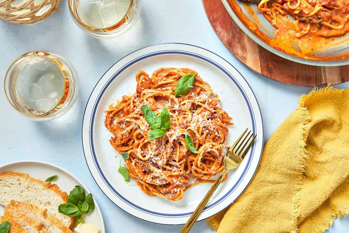 Final creamy tomato pasta plated with fresh basil, grated Parmesan, and olive oil drizzle ready to serve.