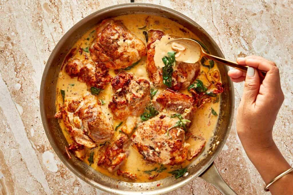 a close up shot with a spoon top down of a creamy brown sauce and golden baked chicken swimming in the sauce