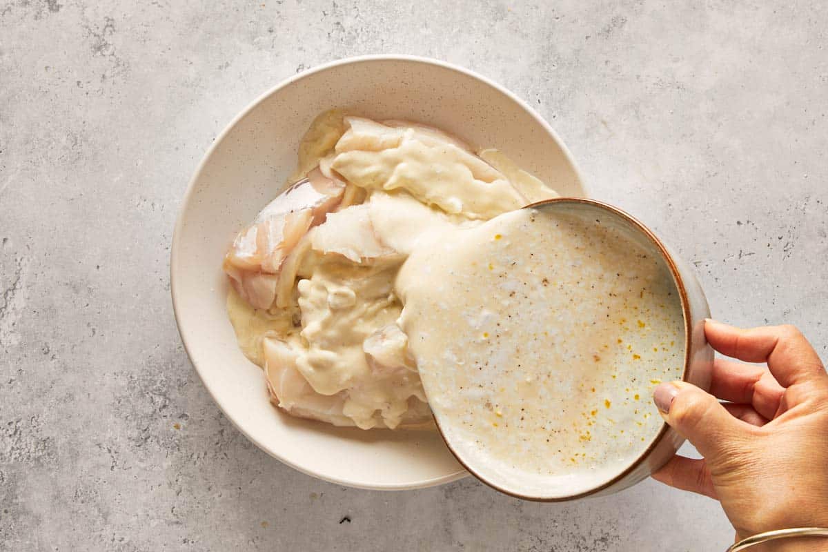 Hand pouring marinade over raw fish fillets in a bowl