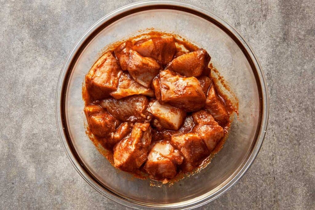 a top down view of chicken cuts in the mix in a glass bowl.