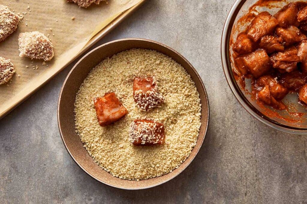 a top down view of a bowl of bread crumbs and pieces of marinated chicken inside ready to be coated in crumbs