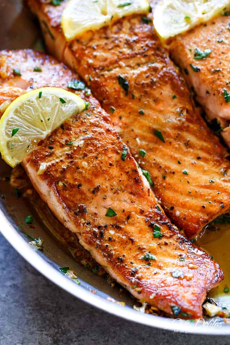 Close up image of salmon in pan with lemon and herbs on top.