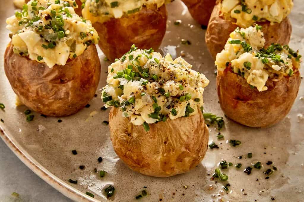 Deviled potatoes filled with creamy egg and potato mixture, topped with chives, pickles, and black pepper, served on a plate
