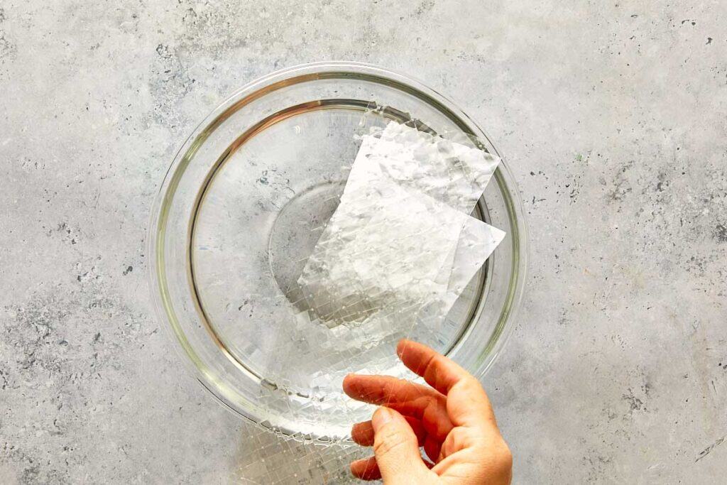more gelatin sheets being melted in a clear mixing bowl of water.