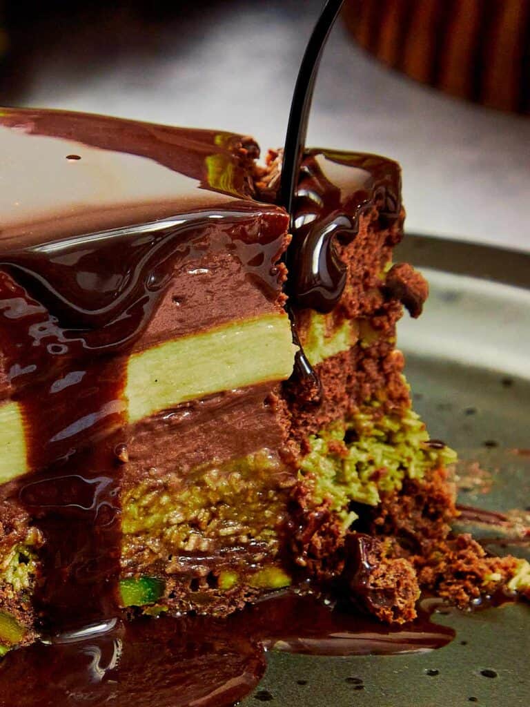 good slice of dubai chocolate cake with chocolate glaze being poured on a wedge that has been cut out, you can see 4 distinct layers of cake