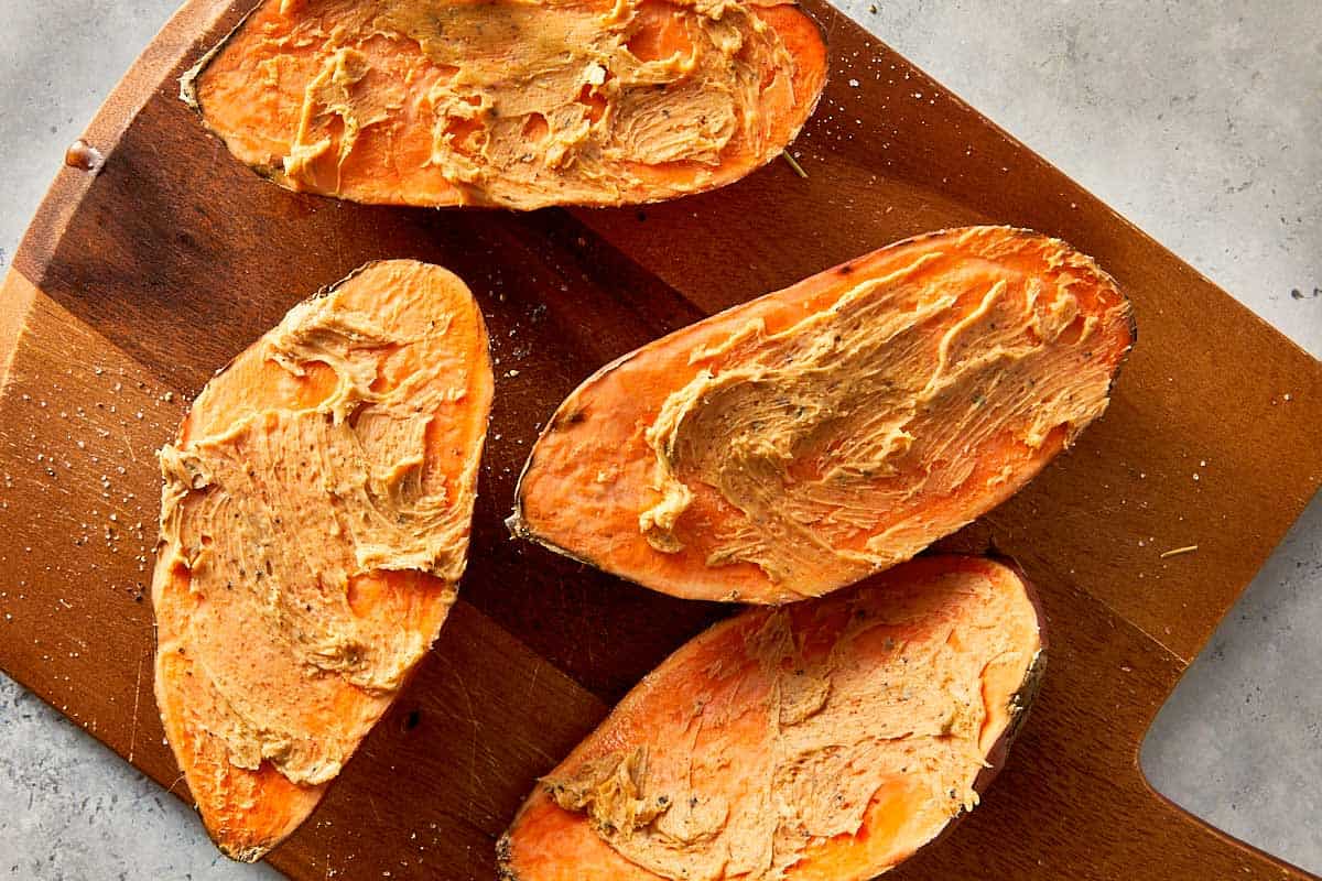 Baked sweet potatoes cut open and spread with garlic butter on a wooden board