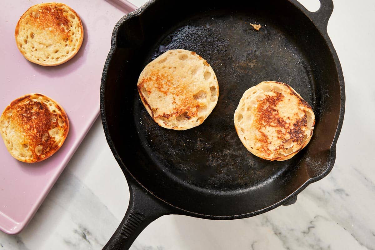 Toasted English muffins in a hot skillet, golden brown on the cut side.