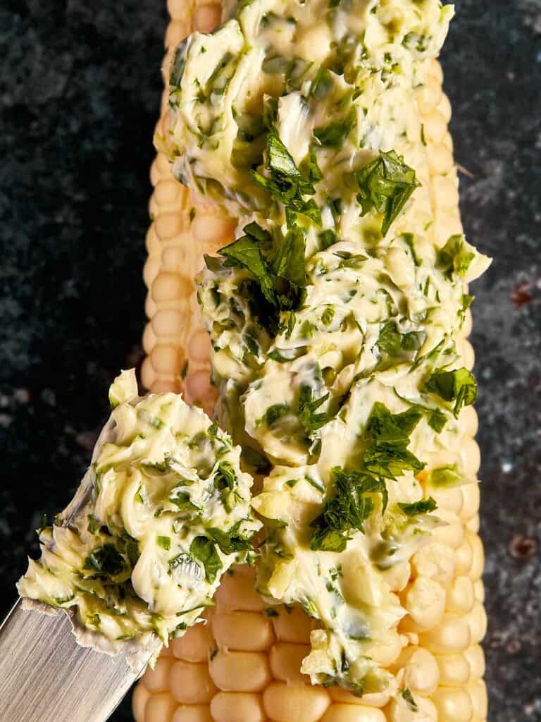 a top down shot of a corn cob with garlic butter smothered on top using a brush