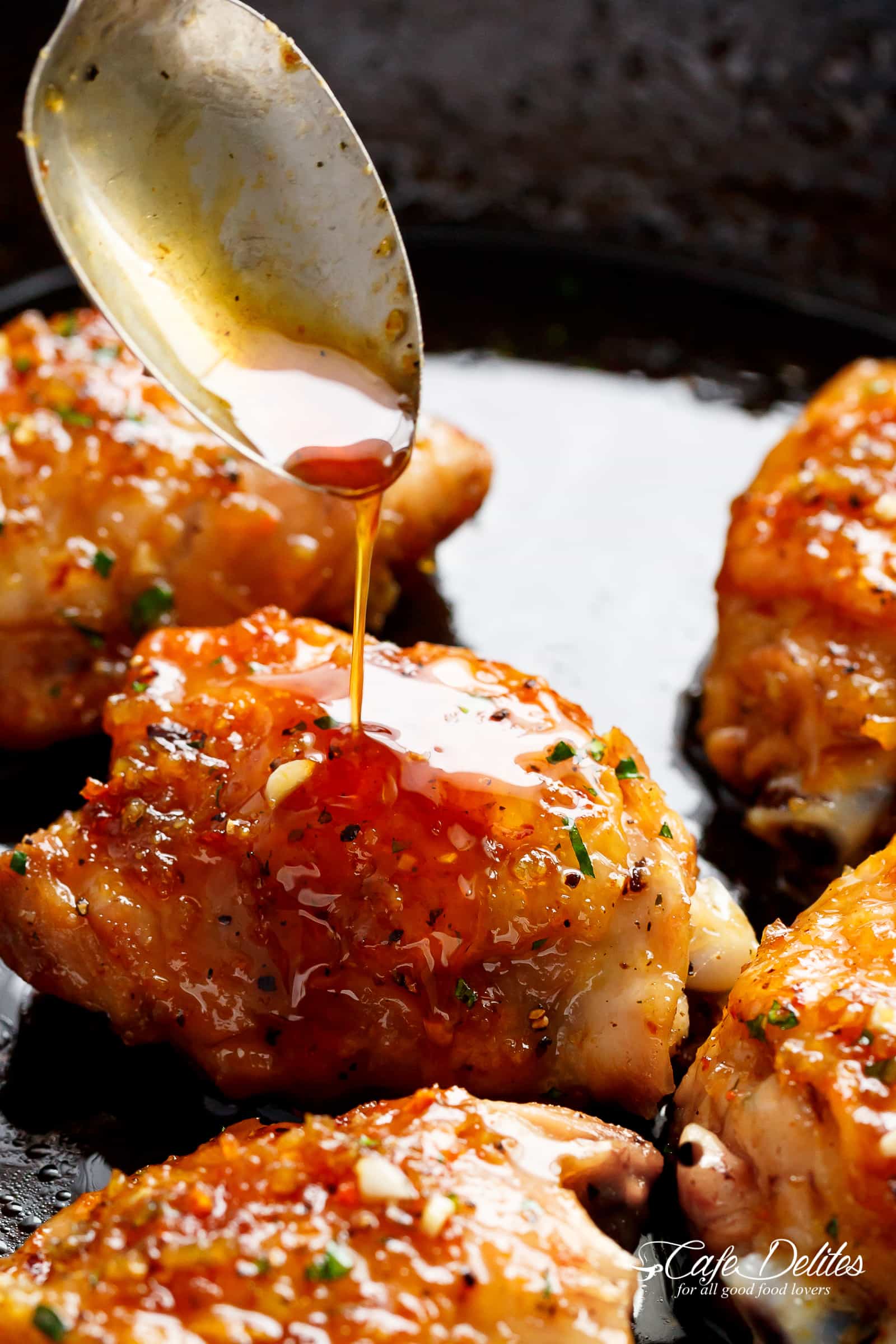 A silver spoon pouring sauce onto a crispy chicken thigh in a pan, looks good