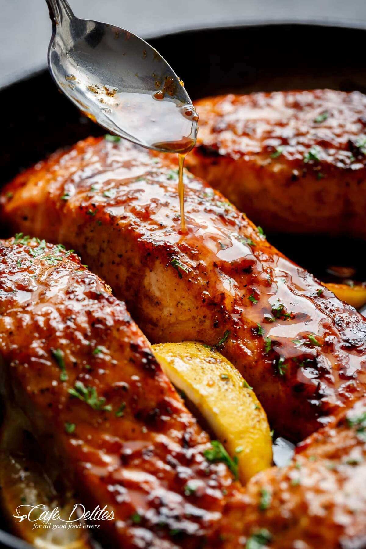 An good close-up shot of the salmon fillets coated in honey garlic sauce, sprinkled with basil, and accompanied by a slice of lemon.