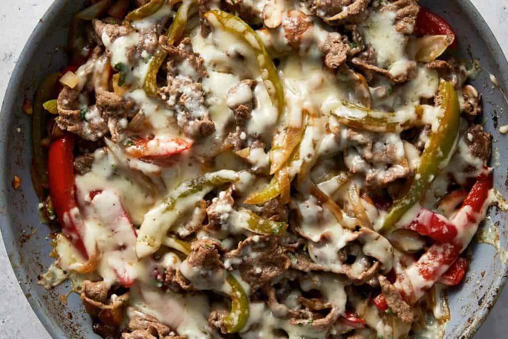 One pan Philly cheesesteak skillet with tender sliced beef, sautéed onions, red and green bell peppers, and mushrooms, finished with melted mozzarella and pecorino cheese.
