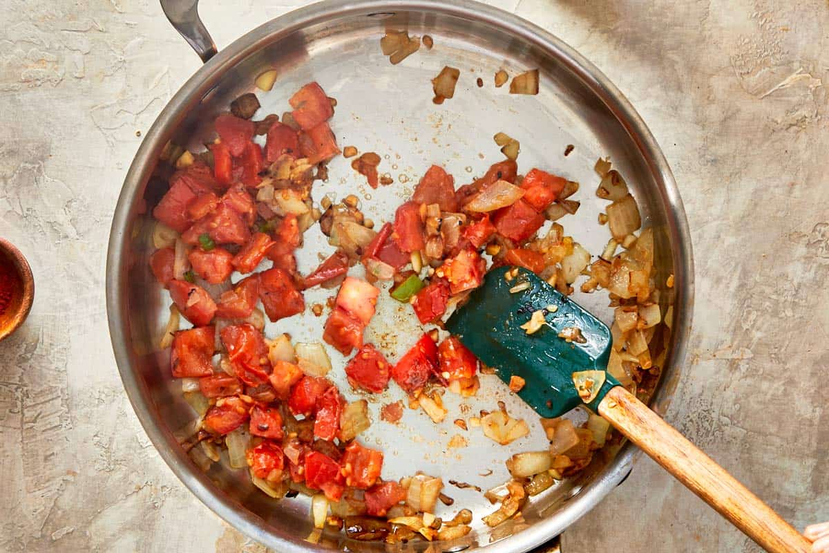 Chopped onions and tomatoes being sautéed in a skillet.
