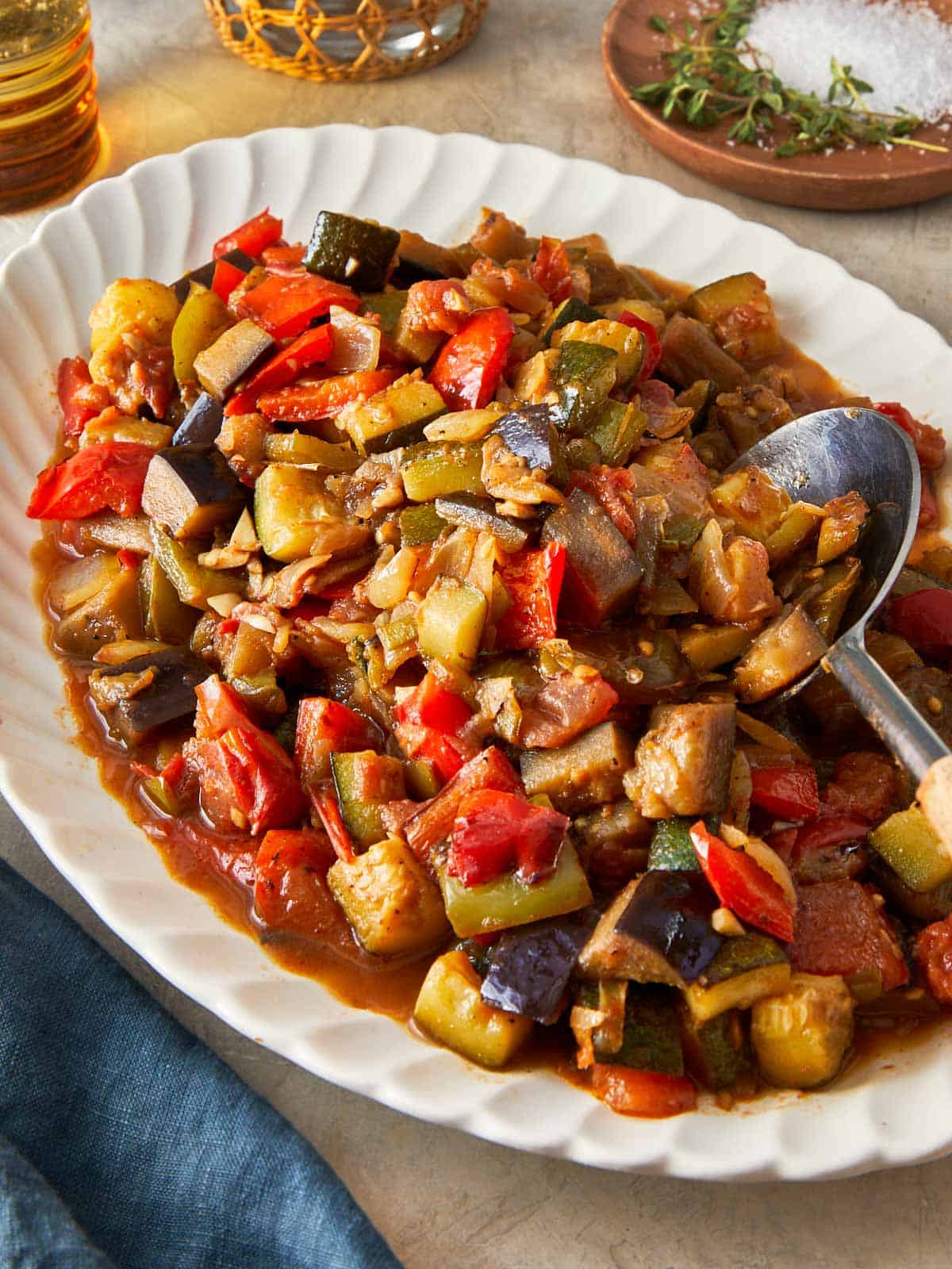 A serving of Ratatouille featuring assorted vegetables, accompanied by a spoon and a glass of red wine.