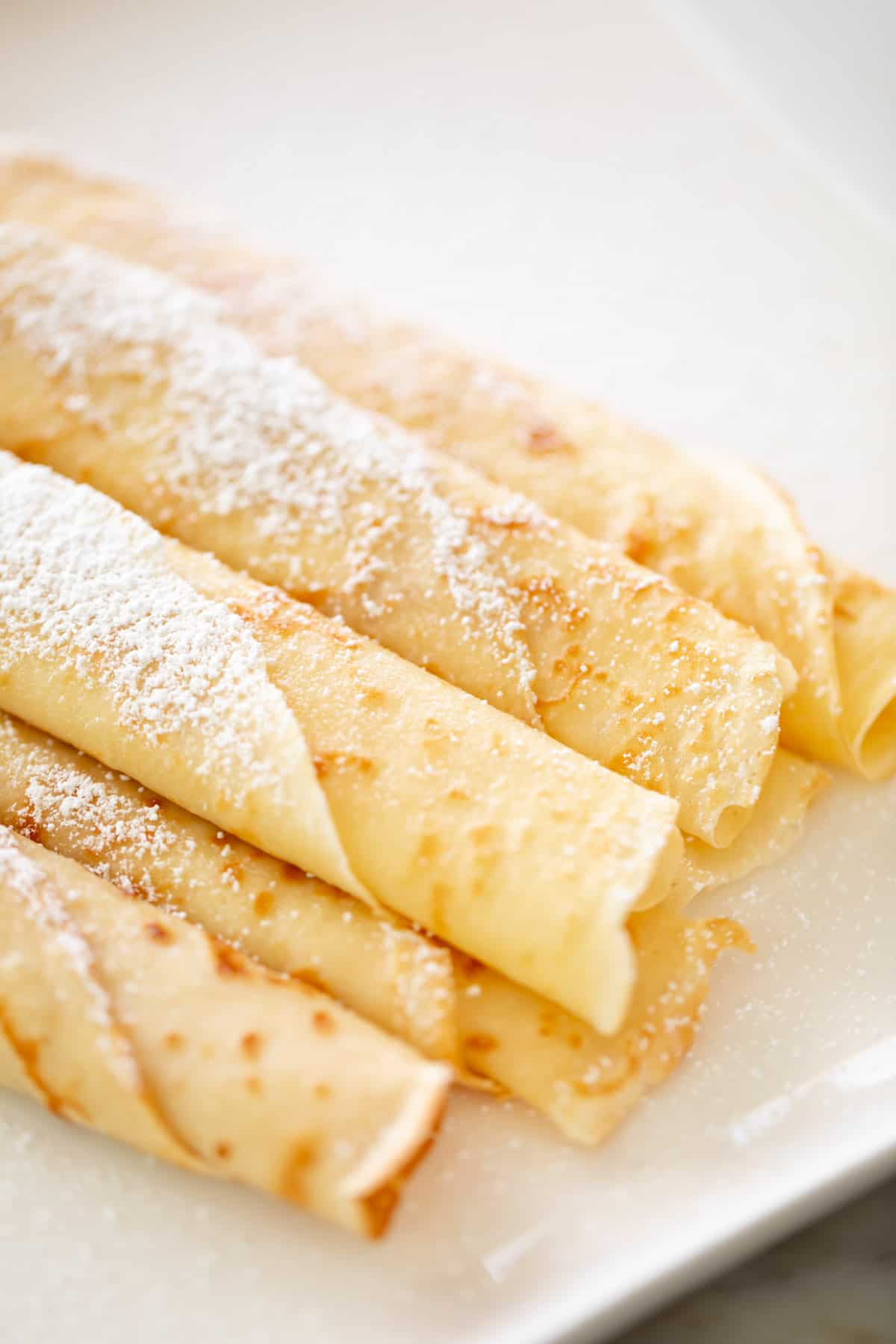 top view image of Rolled up crepes on a plate with confectioners sugar.
