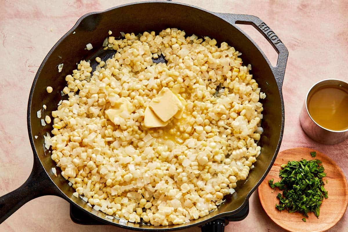 A skillet filled with golden corn kernels and melting butter.