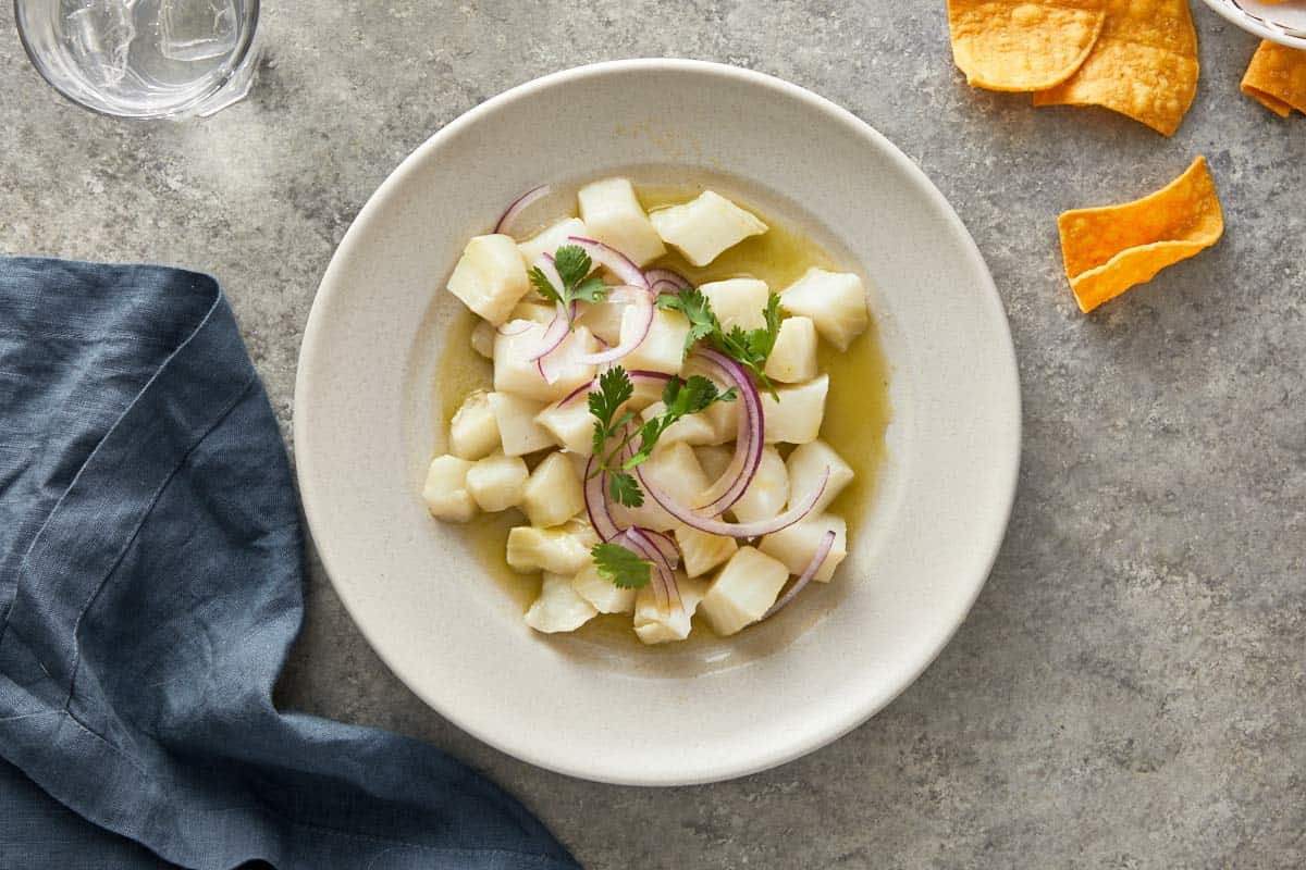 Ceviche served in a shallow bowl topped with red onion and coriander leaves.