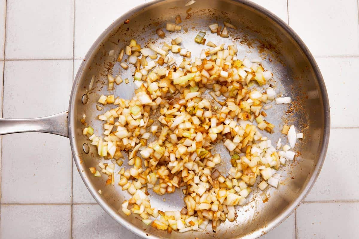 Diced onions sautéing in a stainless steel skillet, starting to caramelize.
