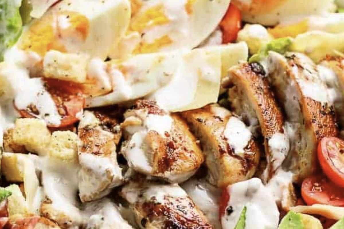 Slice the chicken and chop the bacon. In a bowl, combine romaine lettuce, avocado, tomatoes, parmesan, and croutons. Top with chicken, bacon, and eggs, drizzle with dressing, toss gently, and serve.