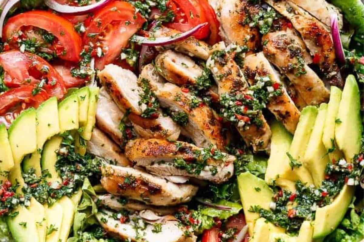 Layer lettuce, tomatoes, onion, and avocado on a plate. Add sliced chicken, drizzle with the chimichurri dressing.