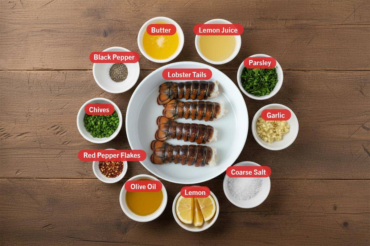 Top shot of ingredients: butter, lemon juice, parsley, garlic, coarse salt, lemon, olive oil, red pepper flakes, chives, black pepper, and lobster tails.