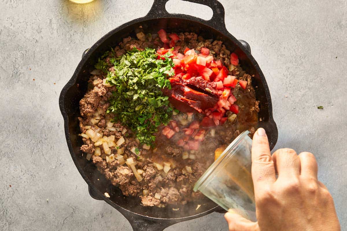 Cooked ground beef with tomatoes, tomato paste, and cilantro in a skillet