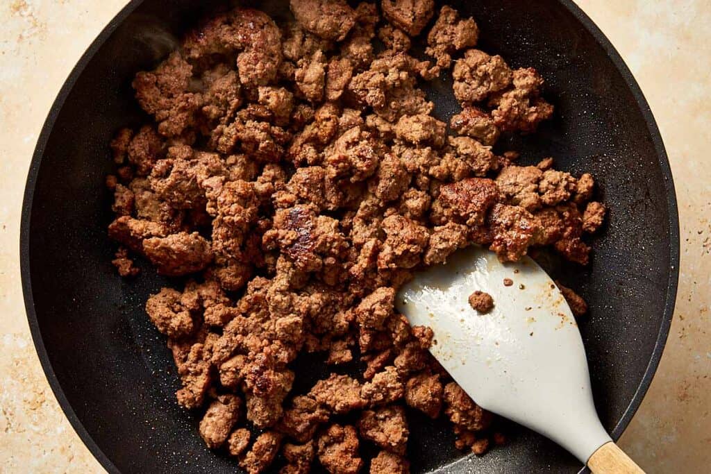 Cooked ground beef browned and crumbled in a skillet with a spatula.