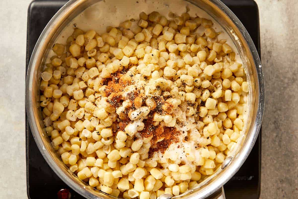 Frozen corn added to a creamy base with salt, black pepper, sugar, and nutmeg, ready to simmer until tender